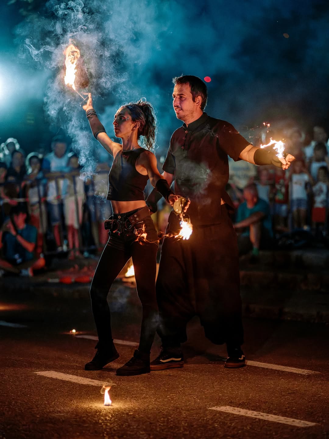 Two fire performers with lit torches in front of an outdoor crowd