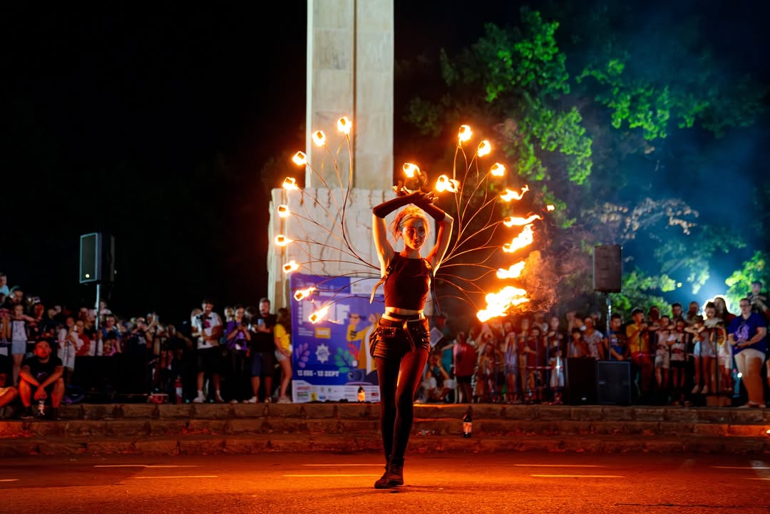 Fire dancer with lit fans spread behind her, facing the audience