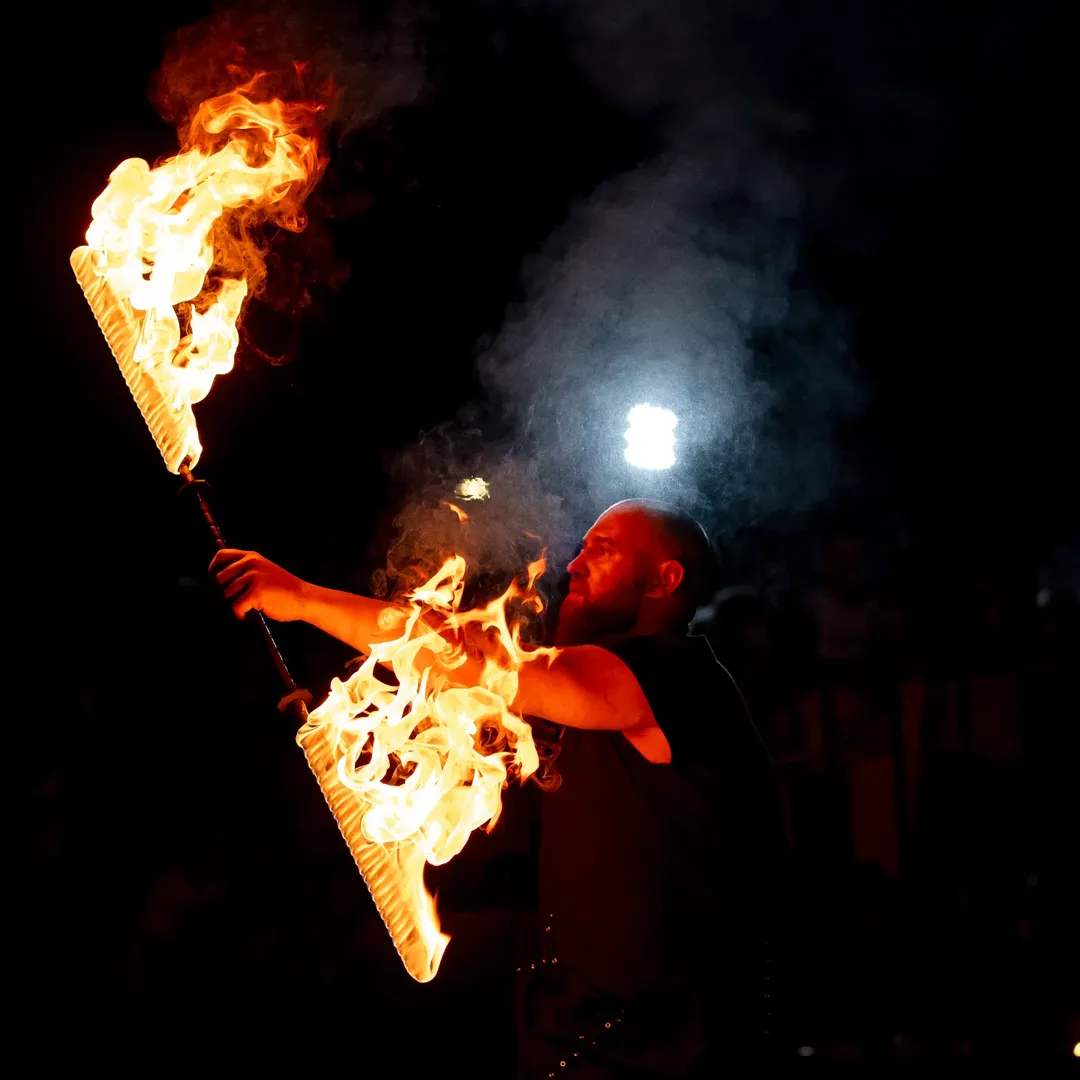 Performer with two fire fans mid-movement against a dark background